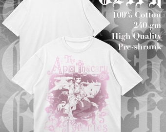 Op de afbeelding: Een wit t-shirt met korte mouwen en een roze grafische print van personages uit The Apothecary Diaries. Het shirt is gemaakt van 100% katoen, 240 gm, en is voorgekrompen. De tekst GLYPH is zichtbaar in de rechterbovenhoek van de afbeelding.