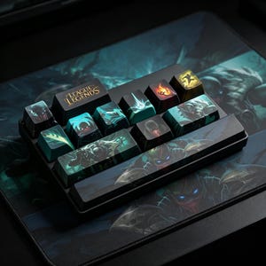 May include: A set of black mechanical keyboard keycaps featuring League of Legends character graphics and logos. The keys display various teal, green, and yellow illustrations of figures in action, with one key clearly labelled with the League of Legends text.