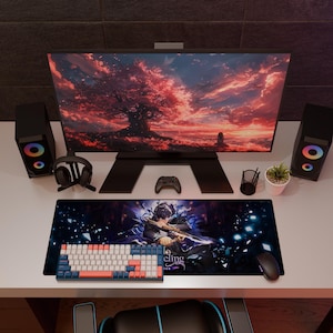 Op de afbeelding: Een gaming-opstelling met een monitor met een zonsondergang, luidsprekers en een toetsenbord. Een muis en een muismat met een karakterontwerp staan ook op het bureau. De muismat heeft de tekst "eling".