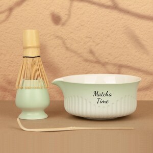 May include: A matcha tea set featuring a light green ceramic bowl with the text "Matcha Time" and a matching whisk holder. A bamboo whisk and scoop are also included, perfect for preparing matcha tea.