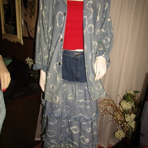 May include: A blue denim jacket with a white cloud pattern and a matching denim skirt with a frayed hem. The skirt has multiple layers and is worn with a red tank top.