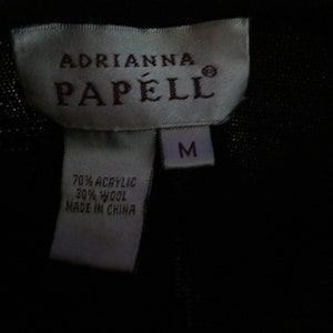 May include: A white tag with black text that reads "Adrianna Papell" and "M" in a smaller font. The tag also includes the fabric content: "70% Acrylic 30% Wool Made in China."