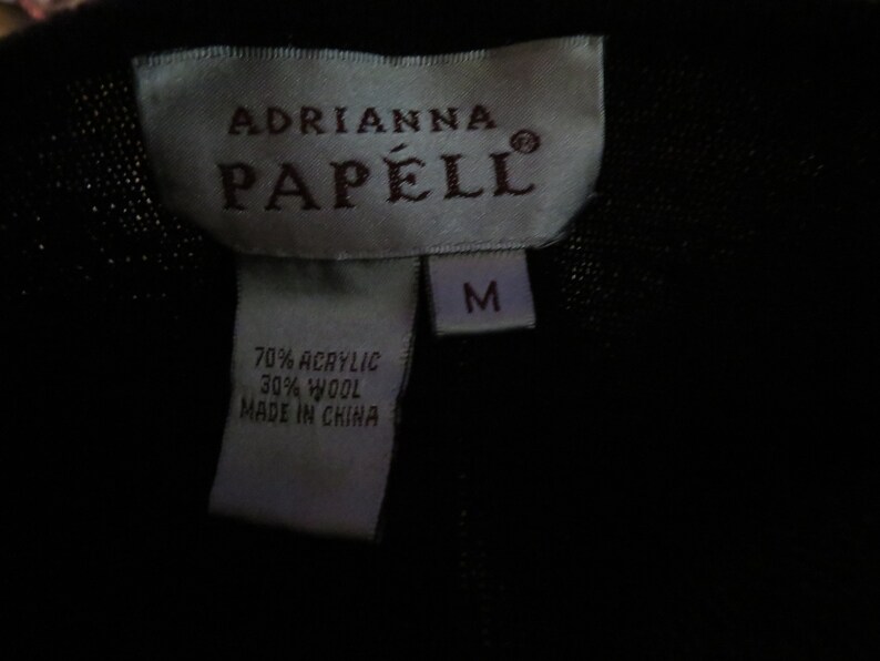 May include: A white tag with black text that reads "Adrianna Papell" and "M" in a smaller font. The tag also includes the fabric content: "70% Acrylic 30% Wool Made in China."