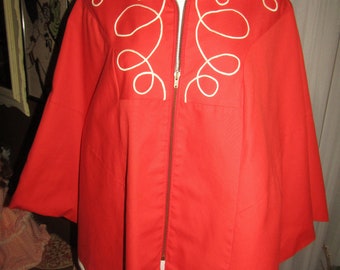 Puede incluir: Chaqueta roja brillante con cremallera frontal y cuello ancho. La chaqueta presenta bordados blancos en espiral en la parte delantera y los hombros. Las mangas son cortas y anchas. La chaqueta se exhibe en un maniquí.