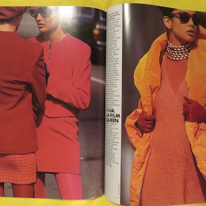 K&ouml;nnte beinhalten: Zwei Frauen in roten und orangen Jacken und Sonnenbrillen. Die Frau links tr&auml;gt einen roten karierten Rock und die Frau rechts tr&auml;gt eine lange orange Jacke mit einem wei&szlig;en Rollkragen darunter. Der Text "VIVA LA FILM QUEEN" ist im Hintergrund sichtbar.