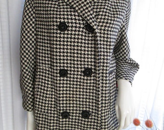 May include: A black and white houndstooth patterned coat with a double breasted closure and black buttons. The coat has a collar and long sleeves.