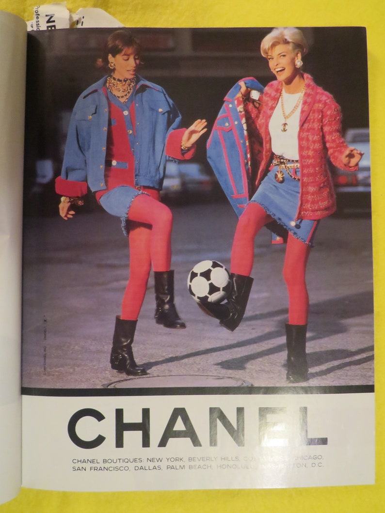 K&ouml;nnte beinhalten: Zwei Frauen in Jeansjacken und R&ouml;cken, rosa Strumpfhosen und schwarzen Stiefeln spielen mit einem Fu&szlig;ball. Der Text "CHANEL" ist in gro&szlig;en schwarzen Buchstaben am unteren Rand des Bildes gedruckt. Der Text "CHANEL BOUTIQUES: NEW YORK, BEVERLY HILLS, CHICAGO, SAN FRANCISCO, DALLAS, PALM BEACH, HONOLULU, WASHINGTON, D.C." ist in kleineren schwarzen Buchstaben unter dem gro&szlig;en Text gedruckt.