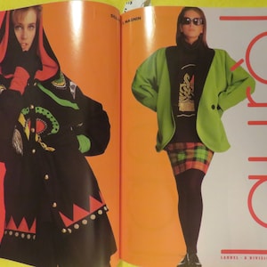 K&ouml;nnte beinhalten: Zwei Frauen pr&auml;sentieren Kleidung. Die Frau links tr&auml;gt eine schwarze und gr&uuml;ne Jacke mit rotem und wei&szlig;em Besatz. Die Frau rechts tr&auml;gt eine gr&uuml;ne Jacke &uuml;ber einem schwarzen Shirt und einem rot-schwarzen karierten Rock. Der Text "LAUREL - A DIVISION OF ESCADA" befindet sich am unteren Rand der Seite.