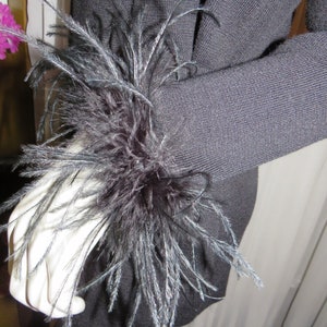 May include: A black sweater with a large black feather embellishment on the sleeve.