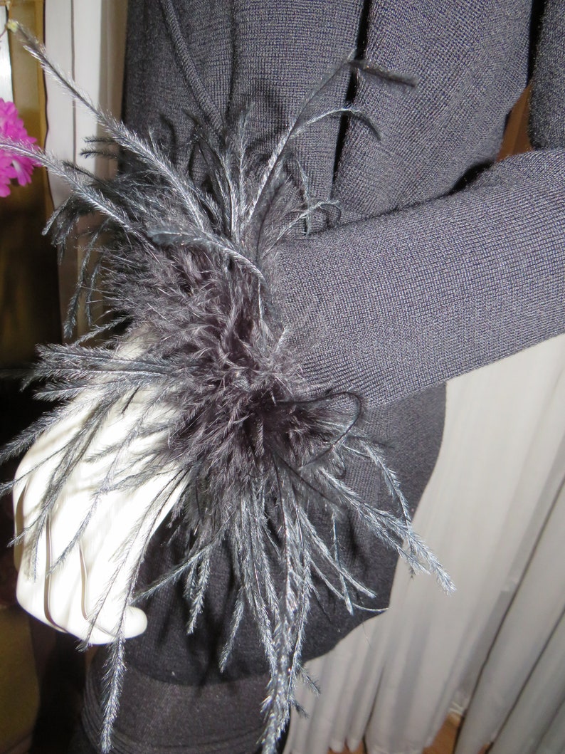 May include: A black sweater with a large black feather embellishment on the sleeve.