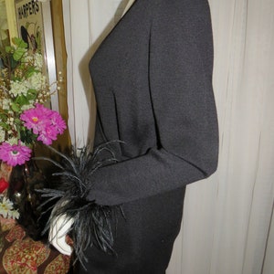 May include: Black long-sleeved sweater with a V-neck and black feather trim on the cuffs.