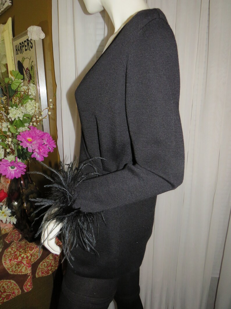 May include: Black long-sleeved sweater with a V-neck and black feather trim on the cuffs.