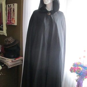 May include: A black hooded cape with a single button closure. The cape is made of a smooth, satin-like fabric.