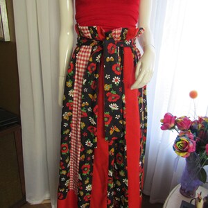 Puede incluir: Una falda roja y negra con estampado floral y patrón de cuadros. La falda tiene una cintura ancha y un lazo en la parte delantera.