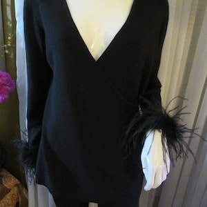 May include: Black long-sleeved sweater with a V-neck and feather trim on the cuffs.