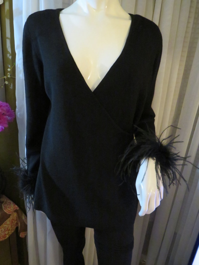 May include: Black long-sleeved sweater with a V-neck and feather trim on the cuffs.