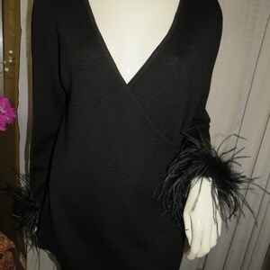 May include: Black long-sleeved sweater with a V-neck and feather trim on the cuffs.