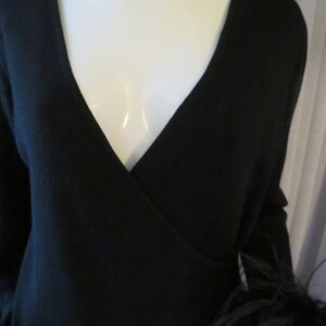 May include: A black wrap sweater with long sleeves and a feather trim on one sleeve.