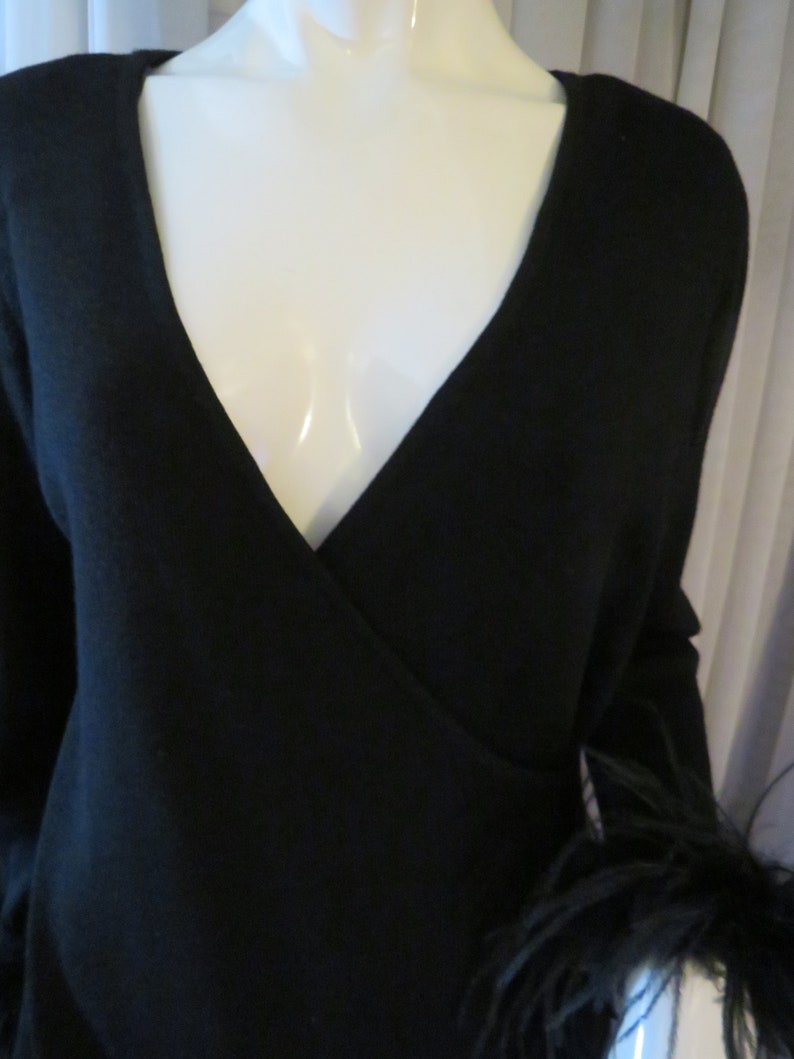 May include: A black wrap sweater with long sleeves and a feather trim on one sleeve.