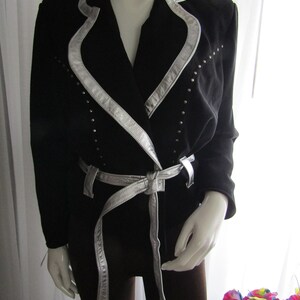 May include: A black blazer with a silver trim and belt. The blazer has a silver trim around the collar and down the front. The belt is also silver and has a buckle.