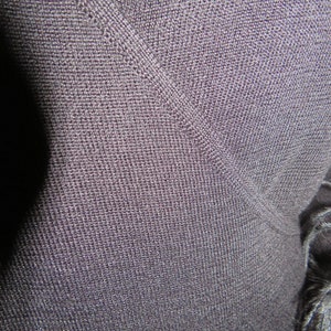 May include: Close-up of a dark gray knit fabric with a V-neckline. The fabric has a fine, textured weave.