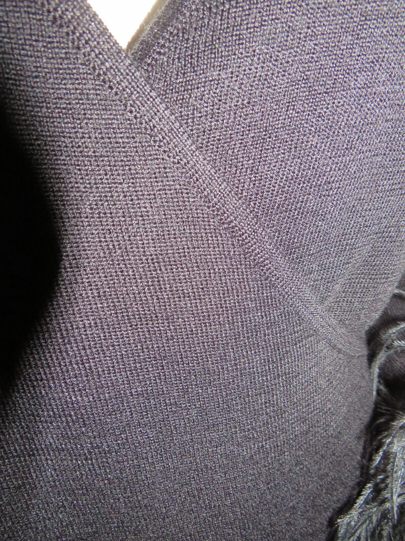 May include: Close-up of a dark gray knit fabric with a V-neckline. The fabric has a fine, textured weave.