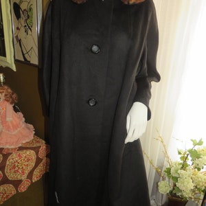 May include: A black wool coat with a large brown fur collar. The coat has a single-breasted closure with two buttons.