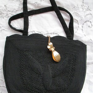May include: A black woven handbag with a scalloped top and a decorative gold pendant. The bag has a detailed woven pattern.