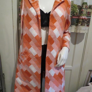 May include: A long, orange and white checkered coat with a collar and long sleeves. The coat has a single button closure and two pockets.