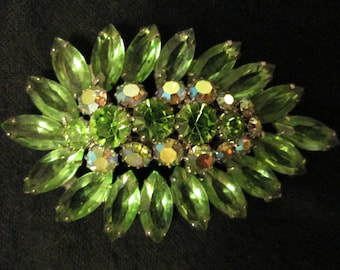 Pode incluir: Broche vintage com design floral. O broche apresenta strass verdes em corte marquise e redondo. As pedras centrais são de um verde vibrante, rodeadas por pedras verdes mais claras e iridescentes, tudo em metal prateado.