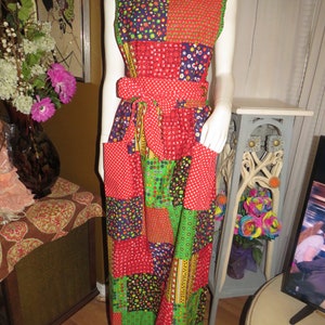 May include: A red, green, and blue patchwork dress with a white polka dot sash. The dress has a sleeveless design and a scoop neck.