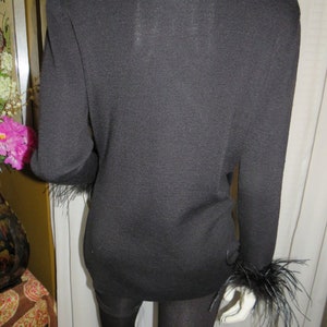 May include: Black long-sleeved sweater with feather trim on the cuffs. The sweater is made of a soft, knit fabric.