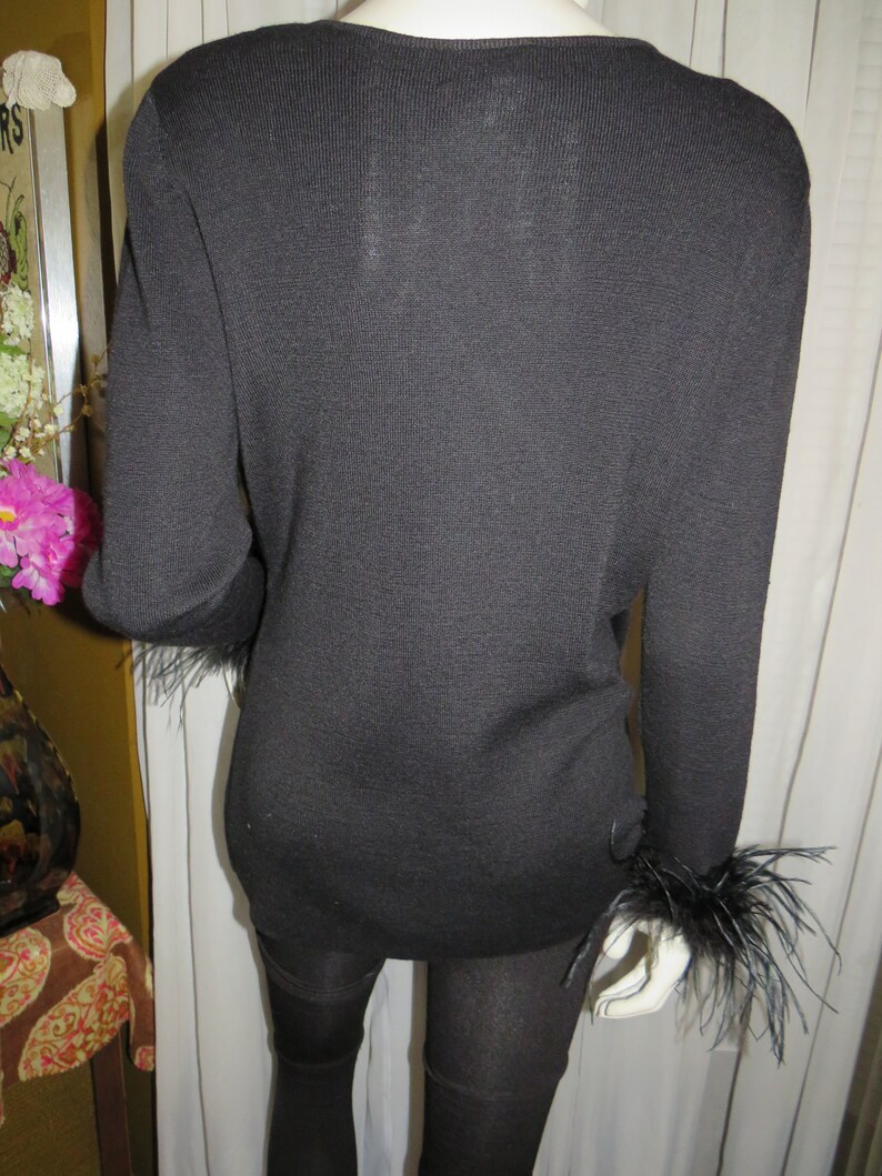 May include: Black long-sleeved sweater with feather trim on the cuffs. The sweater is made of a soft, knit fabric.