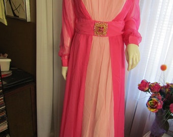 May include: A long pink and light pink chiffon dress with a jeweled belt. The dress has long sleeves and a scoop neckline.