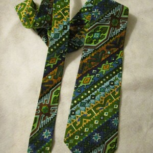 Puede incluir: Una corbata de patrón geométrico verde, azul y marrón. La corbata está hecha de tejido tejido y tiene una punta puntiaguda.