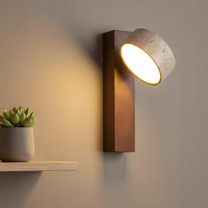 May include: A modern wall-mounted spotlight with a rectangular wooden base and a cylindrical, textured light fixture. The light is angled downward, illuminating the space. The fixture is mounted on a neutral-colored wall.