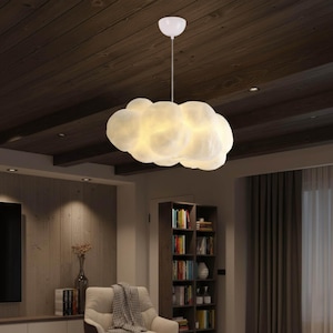 May include: A white cloud-shaped pendant light fixture. The light fixture is suspended from the ceiling by a white cord and a white canopy. The cloud is illuminated from within, creating a soft, warm glow. The fixture is designed for indoor use.