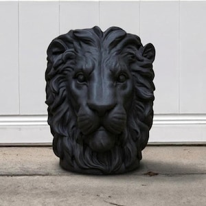 May include: A black lion head sculpture with detailed fur and facial features. The sculpture is made of a dark material and sits on a concrete surface. The lion's gaze is forward, and the mane is intricately carved.