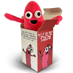 May include: A bright pink plush appendix toy with large white eyes and a black mouth, emerging from a rectangular cardboard box. The box features illustrations of the character and text reading: you don't have to remove your appendix just because you don't know what I do! BUT IF YOU DON'T, I WILL KILL YOU IF THE URGE STRIKES ME!