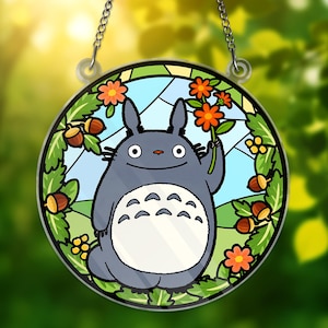 May include: A round stained glass window featuring a cartoon character holding orange flowers. The character is gray with a white belly and large eyes. The window is surrounded by green leaves, acorns, and orange flowers, with a blue sky background.