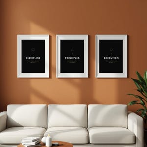 Puede incluir: Tres impresiones artísticas enmarcadas con bordes blancos cuelgan de una pared marrón. Cada impresión tiene un fondo negro con texto blanco y una forma geométrica. Las impresiones dicen "DISCIPLINA", "PRINCIPIOS" y "EJECUCIÓN".
