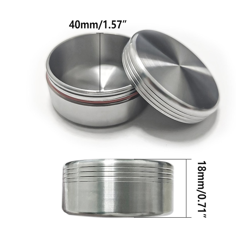 May include: A silver-colored, round container with a lid. The container is 1.57 inches in diameter and 0.71 inches tall. The lid has a ridged design. A red ring is visible inside the container.