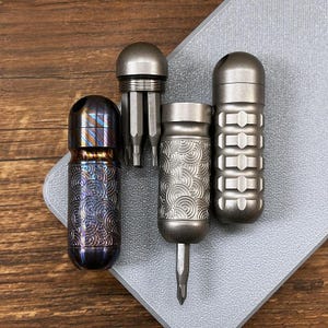 以下が含まれることがあります： 4つの金属製マルチツールのコレクション。ツールは、渦巻き模様やリブデザインなど、さまざまなデザインがあります。ツールはシルバー、ブロンズ、ブルーの色合いです。ツールは灰色の表面に配置されています。