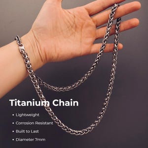 Puede incluir: Una cadena de titanio de tono plateado con un patrón de eslabones trenzados. El texto en la imagen dice: Titanium Chain, Lightweight, Corrosion Resistant, Built to Last, Diameter 7mm. La cadena cuenta con un cierre seguro en el extremo.