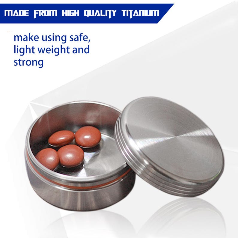 May include: A small, open, round, brushed-metal container with a matching lid. The container holds several brown, oval-shaped pills. Text at the top reads "MADE FROM HIGH QUALITY TITANIUM". The text below reads "make using safe, light weight and strong".