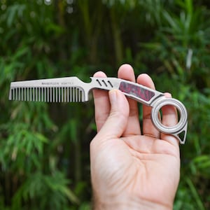 Può includere: Un pettine in metallo color argento con un manico curvo caratterizzato da un inserto marmorizzato rosso e nero. Il pettine presenta un anello per il dito all'estremità ed è inciso con il testo WANERSEN VORTEX. Il design include tre fessure.