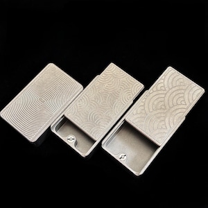 Op de afbeelding: Drie rechthoekige metalen dozen met decoratieve deksels. De deksels hebben verschillende gegraveerde patronen: concentrische cirkels en twee met een golfachtig ontwerp. De dozen zijn open en onthullen de binnenkant. De dozen zijn zilverkleurig.