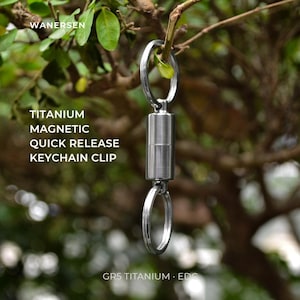 May include: A silver-colored titanium magnetic quick release keychain clip featuring a cylindrical center connector and two circular split rings. The text WANERSEN, TITANIUM MAGNETIC QUICK RELEASE KEYCHAIN CLIP, and GR5 TITANIUM EDC are visible.