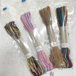 May include: Four skeins of Olympus Sashiko thread in individual plastic packaging, each labeled 20m and 100% cotton. The threads feature variegated color combinations including purple and yellow, pink and white, brown and green, and blue and red.