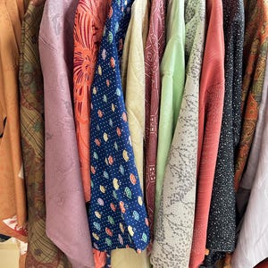 Puede incluir: Una colecci&oacute;n de varios kimonos colgados en un perchero, con diversos colores que incluyen naranja, malva, coral, azul marino con patrones de abanicos, beige, granate, verde claro, gris con estampados florales y negro con motas blancas.